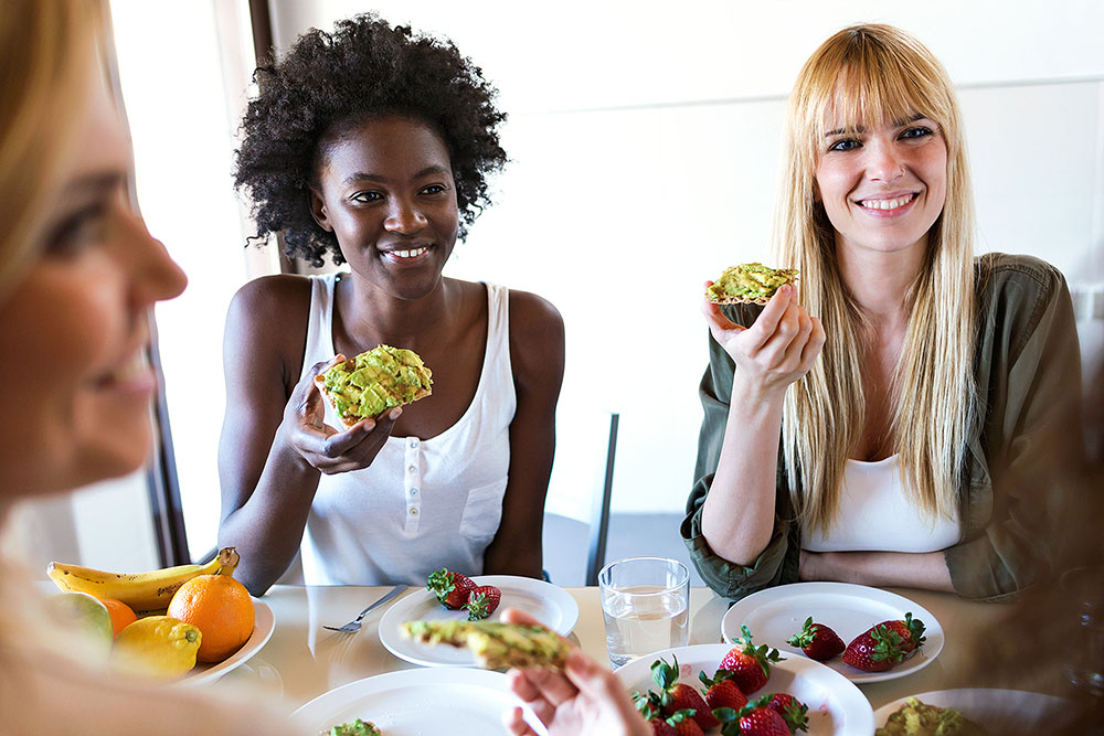 Group of friends laughing and enjoying avocado toast and fresh berries at home.